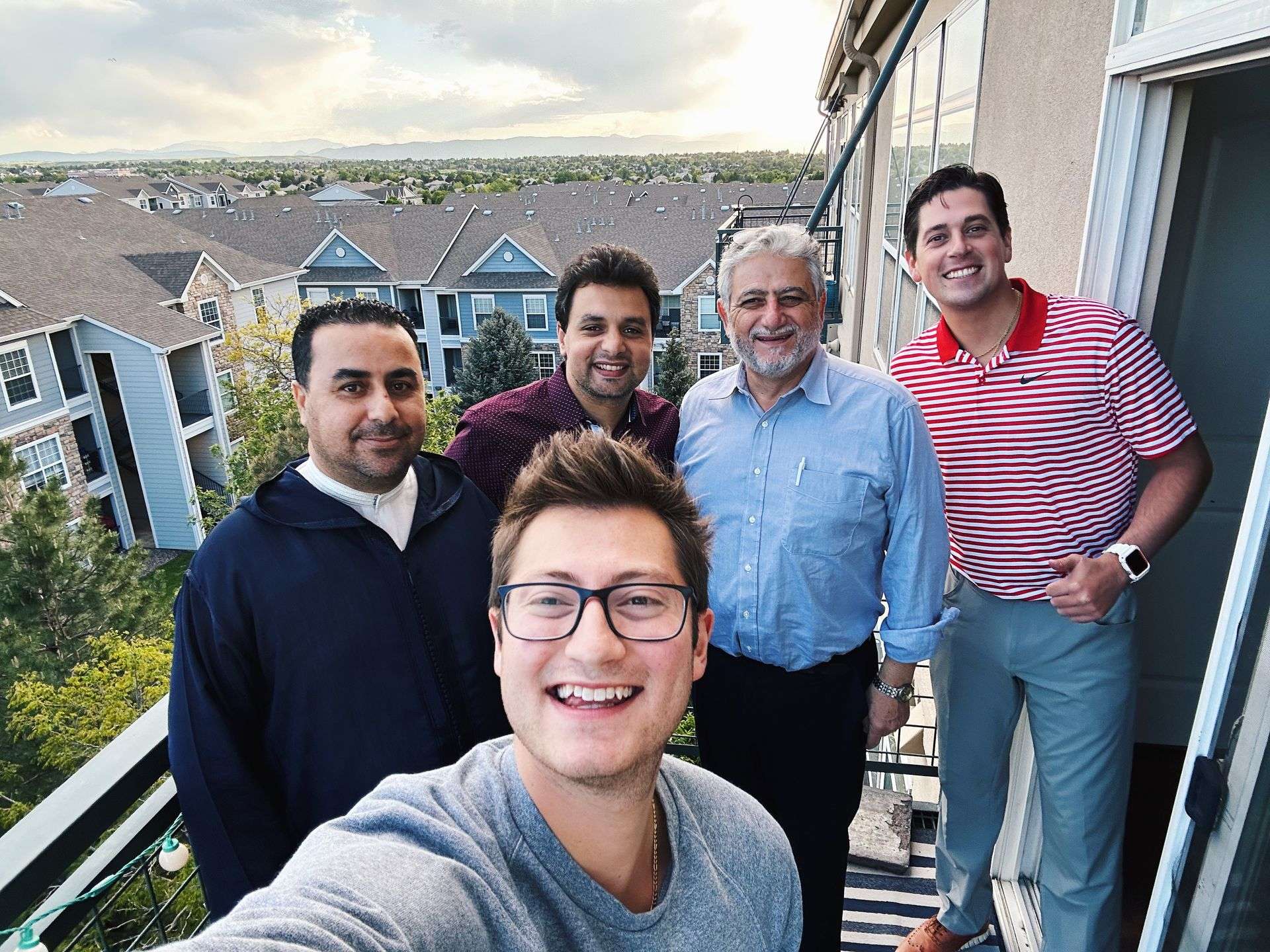 A host and 4 guests stand on an apartment balcony smiling